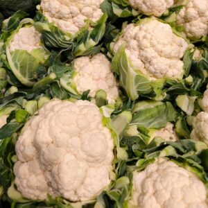 Close-up of fresh cauliflower and broccoli heads with green leaves at market.